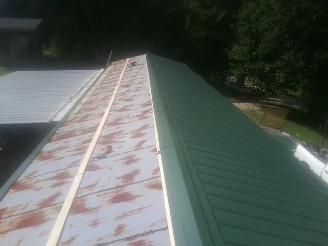 Old rusted panels beside newly installed green metal roofing — Wind Damage Roof Repair by Roofing Brothers in Palm Bay