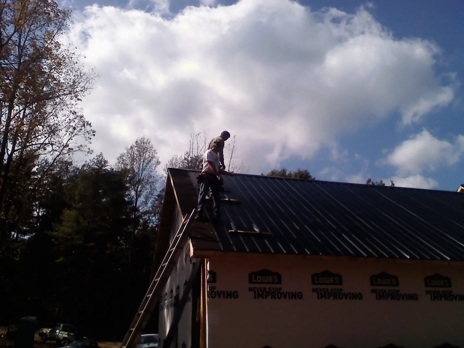 Roofer fastening dark metal panels high against a cloudy sky, from a Roof Inspection job in Palm Bay