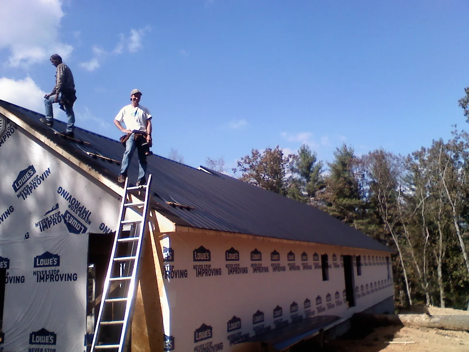 Two roofers standing on a long dark metal roof over a wrapped building in Palm Bay