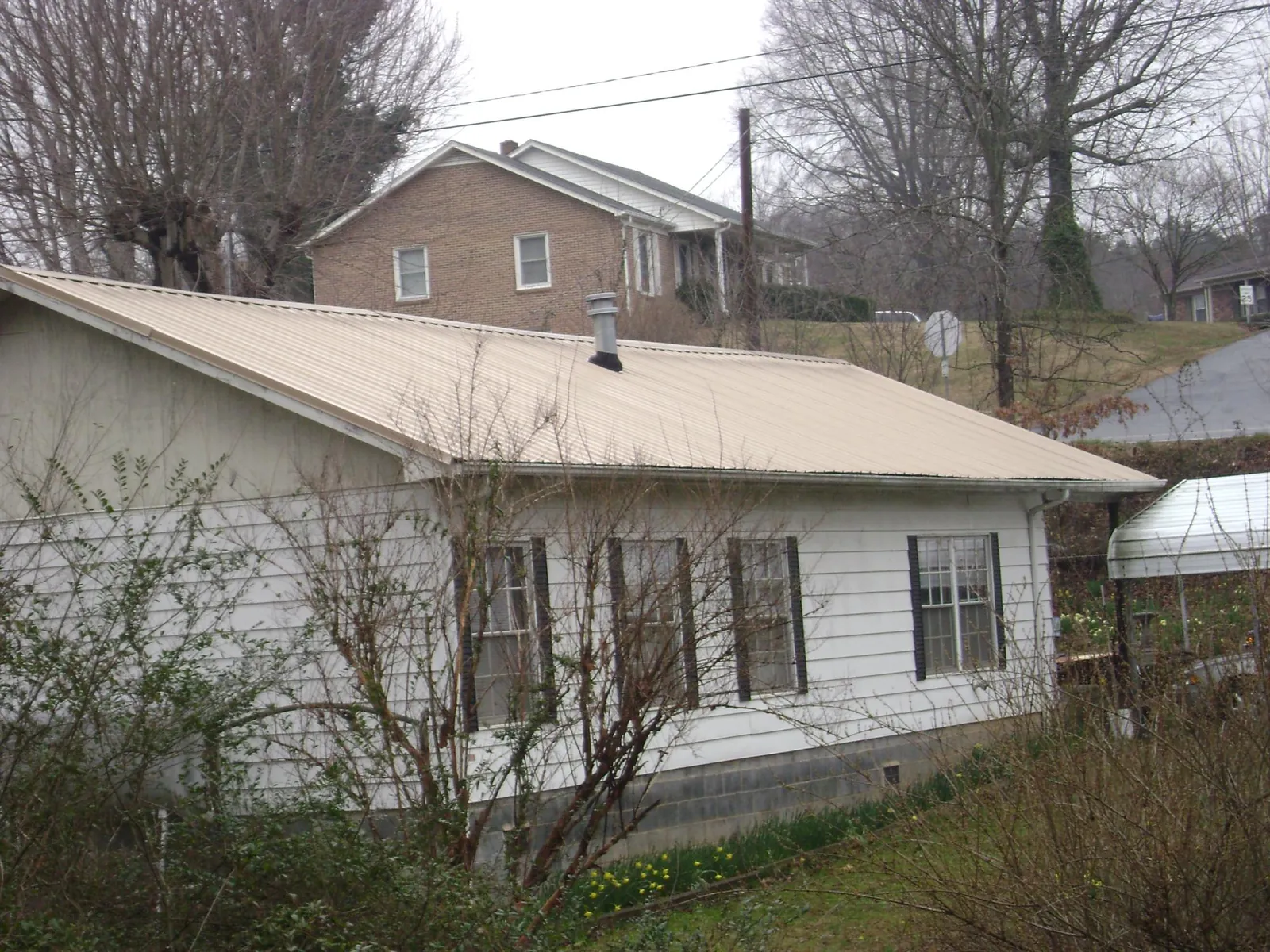Tan metal roof on a white sided house set into a hillside — Commercial Roofing by Roofing Brothers in Palm Bay